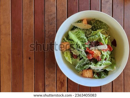 Caesar salad is a healthy menu consisting of lettuce,romaine,croutons,Topped with a dressing that includes lemon juice,olive oil,eggs,grated parmesan cheese,crispy bacon,biscuits serve on wooden table