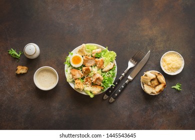 Caesar Salad on dark rustic table, top view, copy space. Homemade chicken caesar salad with grilled croutons.