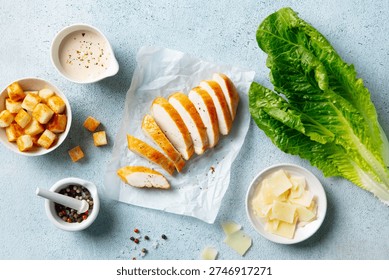 Caesar salad setup: fresh lettuce, grilled chicken, toasted croutons, grated Parmesan, peppered dressing, culinary delight. Blue background. Top view.