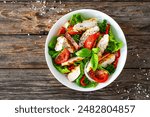 Caesar style salad - delicious grilled chicken breast slices and fresh vegetables and seasonings served in white bowl on wooden table 