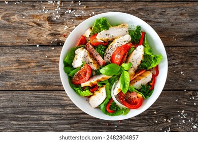 Caesar style salad - delicious grilled chicken breast slices and fresh vegetables and seasonings served in white bowl on wooden table  - Powered by Shutterstock