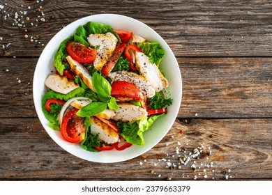 Caesar style salad - grilled chicken breast and fresh vegetables on wooden table