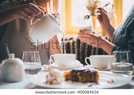 Cafe or bar table with desserts and tea. Two people talking on background. Toned picture