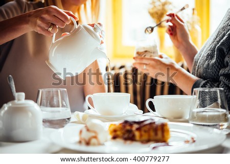 Cafe or bar table with desserts and tea. Two people talking on background.