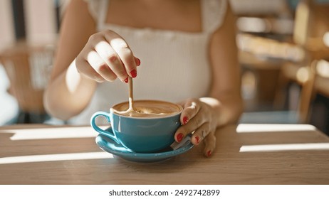 Cafe bliss, young woman enjoys leisurely coffee break, reveling in the sunny interior of a cafeteria, sitting, delicately stirring her drink indoors, closeup showcasing the relaxation - Powered by Shutterstock