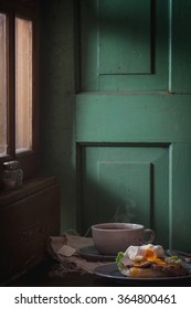 Cafe Breakfast With Homemade Sandwich With Baked Meat And Soft-boiled Egg And Cup Of Hot Pocket Tea Over Dark Wooden Table Near The Window With Turquoise Wall At Background. Dark Rustic Style.