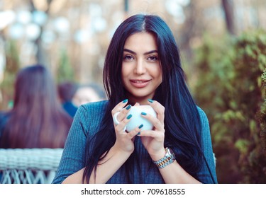 Cafe City Lifestyle. Indian Woman Sitting At The Balcony Terrace Of A Fancy In Coffee Shop Restaurant Holding Cup Of Hot Beverage Tea. Cool Young Modern Female Model. Positive Face Expression Emotion