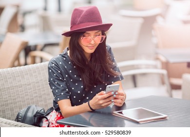 Cafe City Lifestyle Woman On Phone Texting Text Message On Smartphone App Sitting Outdoor In Trendy Urban Cafe. Cool Young Modern Mixed Race Asian Caucasian Female Model In Fashion Retro Look Style