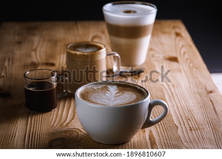 Cafe latte macchiato americano with layers of coffee in a glass coffee cup. Cup of coffee is on a wooden background, top view. Dark background. Low key. Selective focus