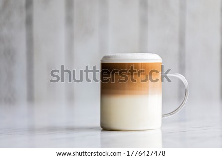 Cafe latte macchiato layered coffee in a see through glass coffee cup. The cup has a white wooden background.