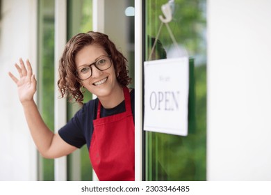 Cafe opening ceremony. Open sign on front door of restaurant or grocery store. Waiter in apron greeting customer. Welcome message on bakery entrance.  - Powered by Shutterstock