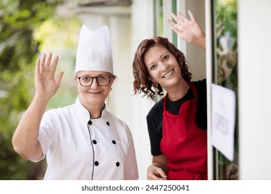 Cafe opening ceremony. Open sign on front door of restaurant or grocery store. Waiter in apron greeting customer. Welcome message on bakery entrance.  - Powered by Shutterstock