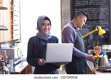 Cafe Owner At His Coffee Shop Counter Using Laptop. Her Partner Working In A Background