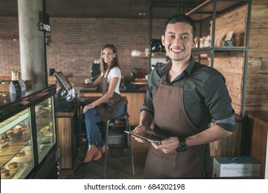 cafe owner at his coffee shop using tablet pc. his partner sitting in a background - Powered by Shutterstock