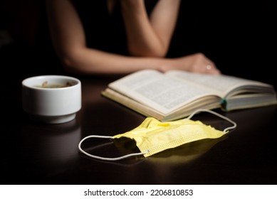 Cafe And Pandemic. Medical Mask, Cup And Open Book. Dark Background. End Of Quarantine.