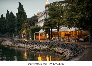 Cafe or restaurant on the shores of Lake Garda at dusk. A cozy cafe with a warm light on the shore of a lake in the mountains. - Powered by Shutterstock