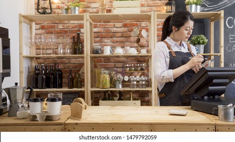 Cafe Store Staff Woman Standing At Billing Counter Noting Customer Orders. Restaurant Owner Taking Notes Writing On Paper With Pen In Vintage Coffee Shop. Waitress In Apron Concentrated Working.