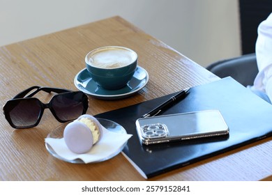 Cafe table with coffee and donut, notebook, smartphone and sunglasses.