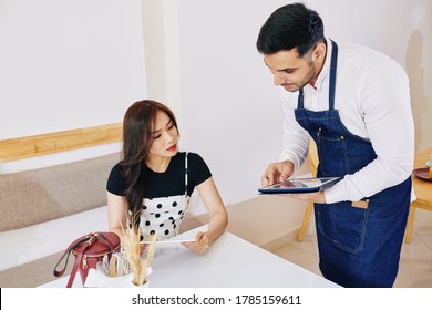 Cafe waiter using tablet computer when writing down order of pretty Asian woman