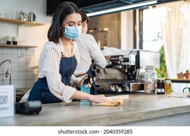 Cafe waiter wear mask, clean restaurant with sanitizer to open store. Asian attractive young couple disinfecting, wiping and rubbing on counter in restaurant before reopen store after Covid19 lockdown - Powered by Shutterstock