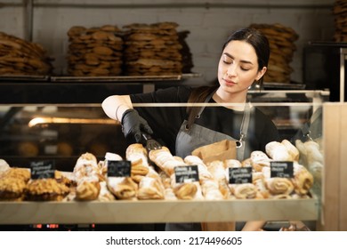 Cafe waitress girl puts fresh pastries on the cafe showcase, bread bakery worker