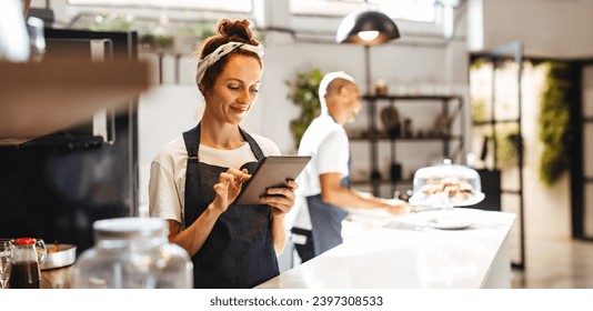 Cafe waitress using a digital tablet to manage orders. Woman using a touchscreen device that helps her to view and organize orders effectively, ensuring prompt and efficient service for the customers. - Powered by Shutterstock