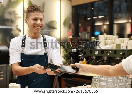 Cafe worker taking payment from client via terminal indoors