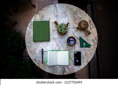 Cafe Workspace table with tea set, notebook smartphone, and plants on marble tabletop