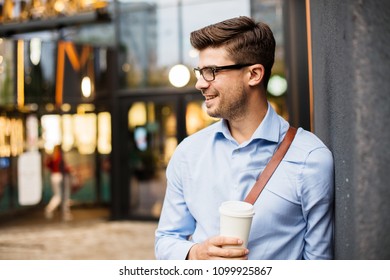 Caffee Break. Handsome Smart Casual Man With Eyeglasses And Leather Bag Having A Take Away Coffee In Urban Area Outside