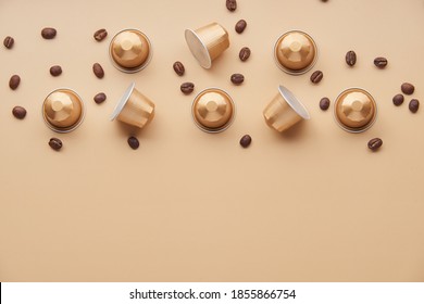Caffeine, hot drinks and objects concept - close up of golden capsules or pods for coffee mashine with some roasted grains on beige background. Top view with space for text. Flat lay..
