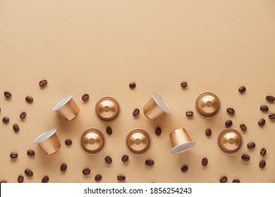 Caffeine, hot drinks and objects concept - close up of golden capsules or pods for coffee mashine with some roasted grains on beige background. Top view with space for text. Flat lay..