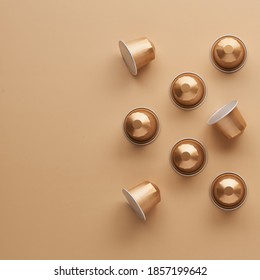 Caffeine, hot drinks and objects concept - close up of golden capsules or pods for coffee mashine on beige background. Top view with space for text. Flat lay..