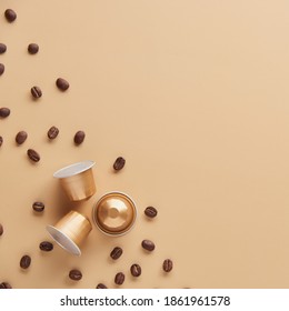 Caffeine, hot drinks and objects concept - close up of golden capsules or pods for coffee mashine with some roasted grains on beige background. Top view with space for text. Flat lay..