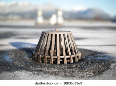 Caged roof drain with defocused vents and winter mountain background. Flat roof with exposed modified bitumen membrane. Inspect and clean roof drain system to prevent water damage. Selective focus.