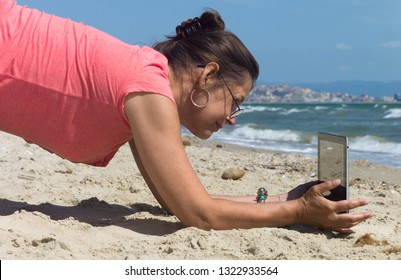 CAGLIARI, SARDINIA - SEPTEMBER 14 2012: Woman With White Pants And Rose Shirt Lies On Her Knees On The Beach In Sardinia And Makes A Photo With Her IPad