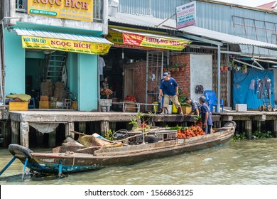 Cai Be, Mekong Delta, Vietnam - March 13, 2019: Along Kinh 28 Canal. Brown Sloop Delivers Red Rambutan Fruits To Retailer-wholesaler Business Quay. People Working.