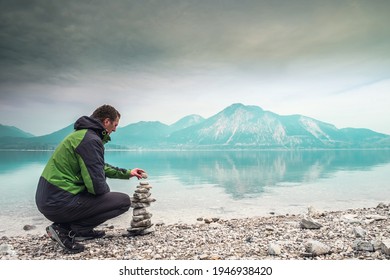 Cairn building. Hiker builds rock cairn from sharp dolomit stones at Alpine lake. Spring in European Alps.