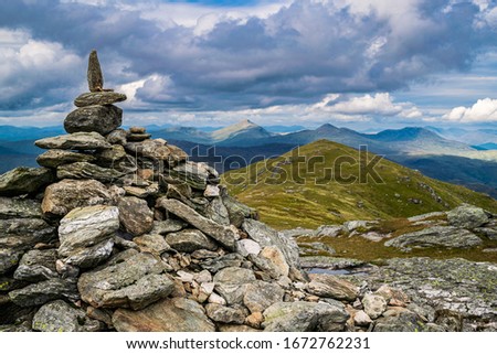 The cairn marking the peak of Ben Vorlich with the scenic Scottish Highlands landscape in the background. 