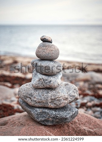 Cairn Pile of stacked red and brown coloured granite stones or pebbles on the beach with grey sea and sky in the background