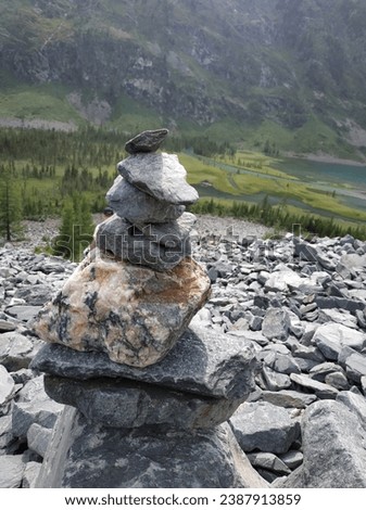 A cairn of rocks, carefully constructed by travelers against the backdrop of a picturesque mountain landscape, symbolizes balance and harmony with nature. The green valley stretching into the distance