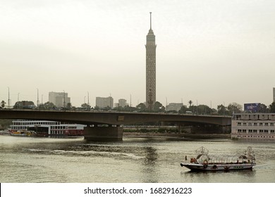 Cairo, Egypt - December 11 2019: A Boat On The River Nile By The 6th October Bridge In Cairo, Egypt. The Cairo Tower, Known As Nasser's Pineapple, Dominates The Urban Landscape.