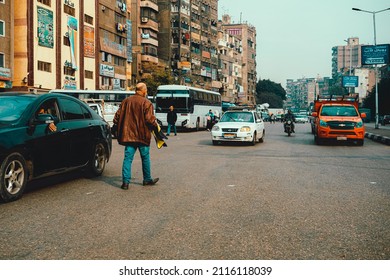 Cairo Egypt December 2021 View Of A Man Walking On The Street Towards The Cars Coming In The Opposite Direction. Symbol Of Going Against The Flow, Poverty In Cairo City