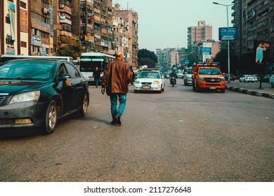 Cairo Egypt December 2021 View Of A Man Walking On The Street Towards The Cars Coming In The Opposite Direction. Symbol Of Going Against The Flow, Poverty In Cairo City