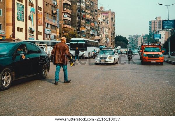 Cairo Egypt December 2021\
View of a man walking on the street towards the cars coming in the\
opposite direction. Symbol of going against the flow, poverty in\
cairo city