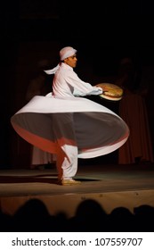Cairo, Egypt - July 3, 2010: A Sufi dancer in white spins and beats a drum during a whirling dervish at an open air courtyard performance at the Al Ghouri in Islamic Cairo