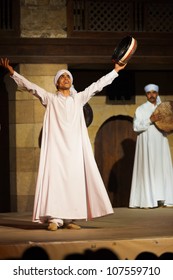 Cairo, Egypt - July 3, 2010: A Sufi dancer in white holding tamborine raising his arms after a whirling dervish at an open air courtyard performance, Al Ghouri, in Islamic Cairo