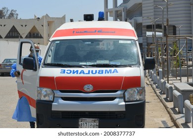 Cairo, Egypt, July 7 2021: Egyptian Health Worker In A Blue Protective Gown, Double Face Mask And Face Shield Beside An Equipped Ambulance Car Ready To Deal With Covid-19 Coronavirus Emergency Cases