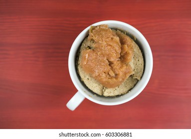 Cake With Applesauce Inside White Cup With Handle, Shot From Above Over Red Wooden Surface Background