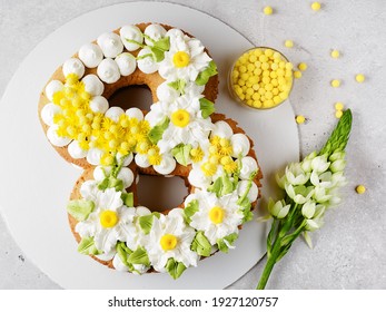 Cake in the form of the number eight for the spring festival. March 8. A cake with a cream decor of daffodils and mimosa. Spring sun on the cake. Dessert and flowers on a gray. Space for text. 