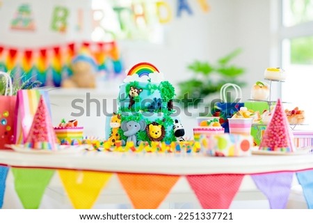 Cake for kids birthday celebration. Jungle animals theme children party. Decorated room for boy or girl kid birthday. Table setting with presents, gift boxes, confetti and sweets. Pastry for child